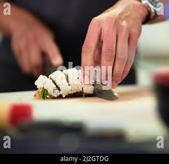 Sieht gut genug aus, um zu essen. Aufnahme eines unidentifizierbaren jungen Mannes, der in seiner Küche Sushi zubereitet. Stockfoto