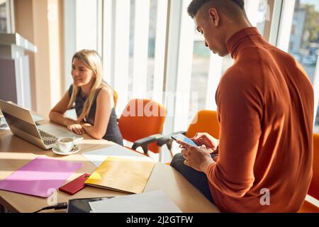 Ein junger Vortragender nutzt ein Smartphone während einer Business-Vortragspause in entspannter Atmosphäre im Konferenzraum. Unternehmen, Mitarbeiter, Unternehmen Stockfoto