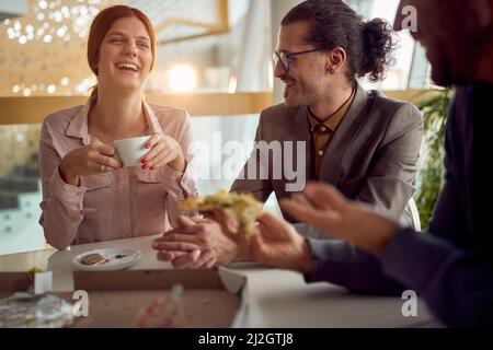 Eine junge, fröhliche Geschäftsfrau hat sich mit ihren männlichen Kollegen während einer Mittagspause in freundlicher Atmosphäre im Firmengebäude gut gelaunt. Stockfoto