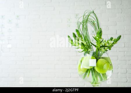 Eine Nahaufnahme der Ornithogalum-Pflanze und der Äpfel in einer großen Glasschale auf einem Tisch Stockfoto