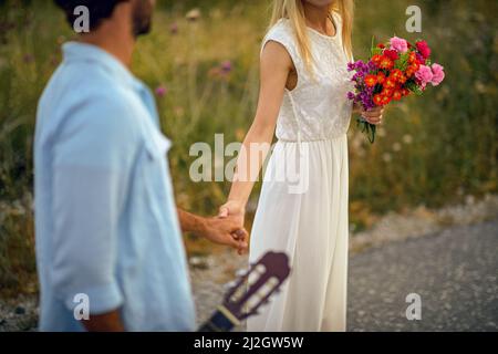 Das Brautpaar im böhmischen Stil hält die Hände und läuft. Bräutigam mit Gitarre. Hochzeitszeremonie, Liebe, Naturkonzept Stockfoto