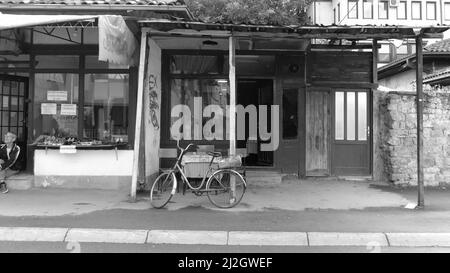 NOVI PAZAR, SERBIEN - 25. JULI 2017: Schwarz-weiß Ansicht Handelsstraße der Arbeiterklasse: Und alte Fahrrad ist Parkplatz vor einer anonymen Taverne ne ne Stockfoto