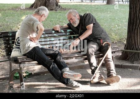 SOFIA, BULGARIEN - 02. AUGUST 2017: Zwei Männer mittleren Alters sitzen auf einer Bank und spielen ein Schachspiel in einem Stadtgarten in der Innenstadt von Sofia Stockfoto