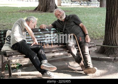SOFIA, BULGARIEN - 02. AUGUST 2017: Zwei Männer mittleren Alters sitzen auf einer Bank und spielen ein Schachspiel in einem Stadtgarten in der Innenstadt von Sofia Stockfoto