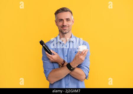 Mann halten elektrische Rasiermesser und Creme auf gelbem Hintergrund, Haut Stockfoto