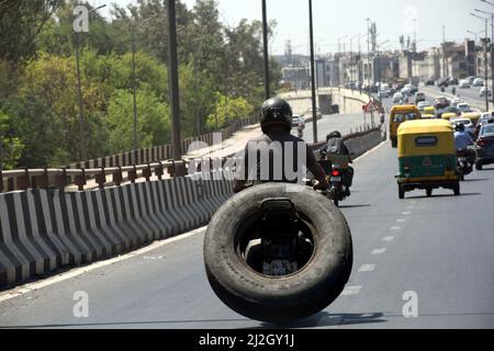 Neu-Delhi, Indien. 01. April 2022. Ein Mann fährt am 1. April 2022 in Neu Delhi, Indien, bei heißem Wetter mit einem riesigen Reifen auf dem Rücken ein Motorrad. (Foto: Ravi Batra/Sipa USA) Quelle: SIPA USA/Alamy Live News Stockfoto