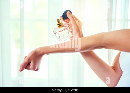 Parfüm - ein unsichtbares, aber unvergessliches Accessoire. Nahaufnahme einer unkenntlichen Frau, die Parfüm auf ihre Handgelenke aufgibt. Stockfoto