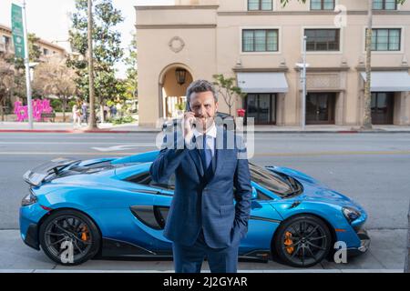 Selbstbewusster Händler spricht auf dem Smartphone neben dem Auto Stockfoto