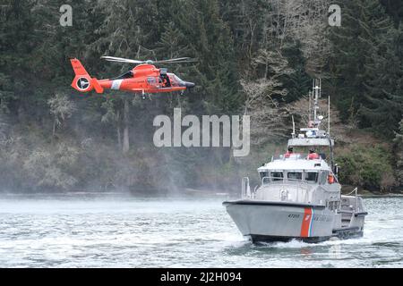 Die Besatzung an Bord eines 47-Fuß-Motorlifeboots von der Küstenwache Umpqua River führt ein Hubtraining mit einer MH-65 Dolphin Helicopter-Besatzung von der Air Station North Bend im Umpqua River in der Nähe von Winchester Bay, Oregon, 15. März 2022 durch. Es werden regelmäßig Schulungsmaßnahmen durchgeführt, um sicherzustellen, dass die Such- und Rettungskapazitäten der Küstenwache dem von ihnen erwarteten hohen Standard entsprechen. Stockfoto