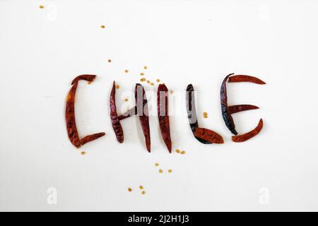 Das Wort Chile wurde auf Spanisch mit trocken gerösteten chilli de Arbol auf einer weißen Oberfläche geschrieben; Capsicum annum; mexikanischer Pfeffer. Stockfoto