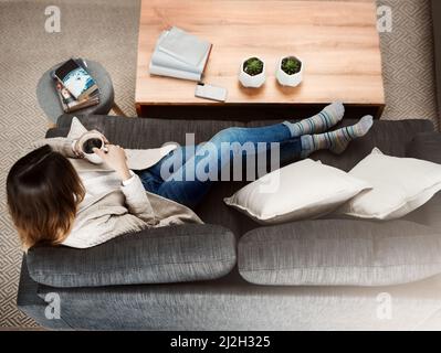 Eine Tasse voller Erinnerungen. Aufnahme einer attraktiven jungen Frau, die auf ihrem Sofa sitzt, während sie sich zu Hause entspannt und Kaffee trinkt. Stockfoto