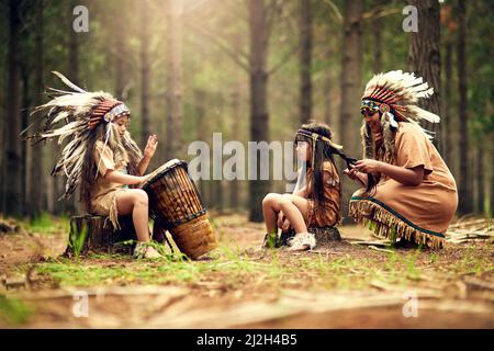 Das Lied ihrer Leute zu spielen. Aufnahme einer jungen Frau und ihrer beiden Töchter, die im Wald Dressup spielen. Stockfoto