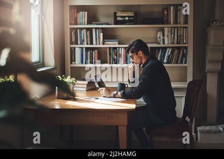 Dies einige sorgfältige Überlegungen. Aufnahme eines jungen Geschäftsmannes, der bei der Arbeit an einem Laptop zu Hause in seinem Büro nachdenklich aussieht. Stockfoto