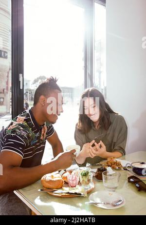 Lächelndes Paar genießt das Frühstück und schaut auf Smartphone im Restaurant Stockfoto