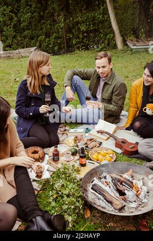 Eine Gruppe von Freunden genießt ein Picknick um die Feuerstelle im Garten Stockfoto