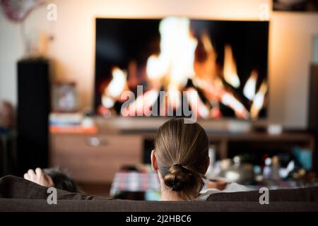 Rückansicht des Mannes, der auf dem Sofa vor dem Kamin sitzt Stockfoto