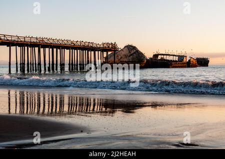 Ein wunderschöner Sonnenuntergang über dem Strand in der Nähe von Aptos, Kalifornien, der den alten, verödnisten Pier und ein altes Schiffswrack hervorhebt. Stockfoto