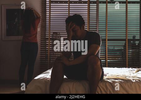 Deprimiertes Ehepaar, Ehemann und Ehefrau, die im dunklen Schlafzimmer mit schwachem Licht Kopf in den Händen auf dem Bett sitzen, dramatisches Konzept Stockfoto