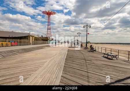 Strandpromenade mit rotem Fallschirmsprung, Luna Park Vergnügungspark auf Coney Island, Brooklyn, New York City an sonnigen Wintertagen mit bewölktem Himmel, PE Stockfoto