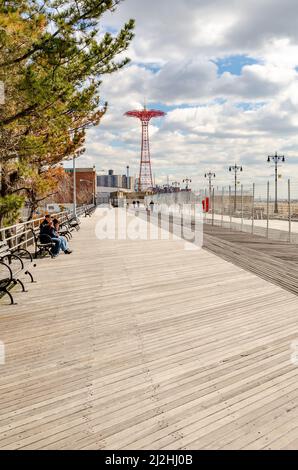 Strandpromenade auf Coney Island, Promenade mit vielen Bänken, roter Fallschirmsprung im Hintergrund, Brooklyn, New York City während des sonnigen Wintertages Stockfoto