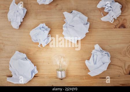 Schreibblöcke. Hochwinkelige Aufnahme einer Glühbirne, die von zerknittert auf einem Schreibtisch umgeben ist. Stockfoto