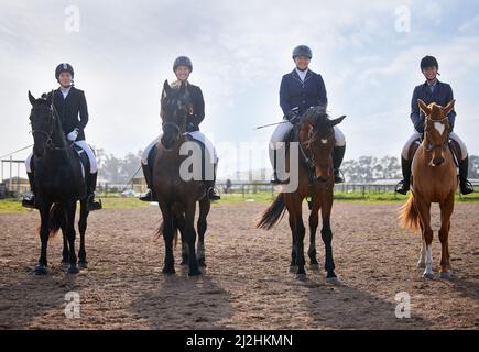 Sie teilen die Liebe zum Reiten. Ganzkörperaufnahme einer Gruppe attraktiver junger Jockeys, die auf dem Bauernhof ihre Pferde reiten. Stockfoto