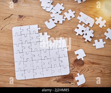 Kein Stück verraust. High-Angle-Aufnahme eines unfertigen Puzzles, das auf einem Holztisch liegt. Stockfoto