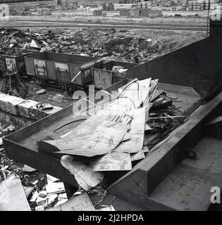 1950s, historische, Stahlschrott-Bleche auf einem Eisenbahnseitenhof mit anderen Metallschrott saßen neben den Güterwagen im Stahlwerk Abbey Works, Port Talbot, Wales, Großbritannien. Die meisten Metallabfälle, einschließlich Eisen und Stahl, können recycelt und wiederverwendet werden. Stockfoto