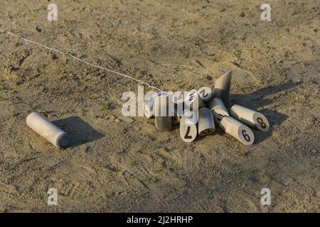 Molkky-Kegeln breiteten sich auf dem Sandboden einer Bowlingbahn aus, nachdem der Stock daneben geworfen wurde Stockfoto