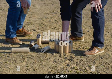 Zwei Senioren, die die Kegel des Molkky-Spiels auf dem sandigen Boden einer Bowlingbahn zurücklegen Stockfoto