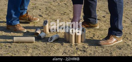 Banner von zwei Senioren, die die Kegel des Molkky-Spiels auf dem sandigen Boden einer Bowlingbahn zurücklegen Stockfoto