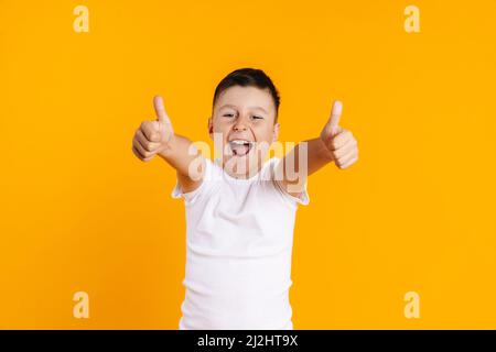 Glücklich lächelnder präteen Junge in T-Shirt stehen über gelbem Hintergrund geben Daumen nach oben Stockfoto