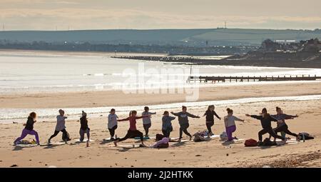 Portobello, Edinburgh Schottland, Großbritannien. April 2022. Erste Beach Yoga Klasse von 2022 am Meer neben dem Firth of Forth. Die Temperatur beträgt etwa 5 Grad Celsius, aber die Sonne gab der harten Gruppe Wärme. Stockfoto