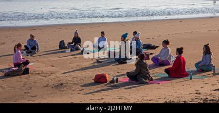 Portobello, Edinburgh Schottland, Großbritannien. April 2022. Erste Beach Yoga Klasse von 2022 am Meer neben dem Firth of Forth. Die Temperatur beträgt etwa 5 Grad Celsius, aber die Sonne gab der harten Gruppe Wärme. Stockfoto