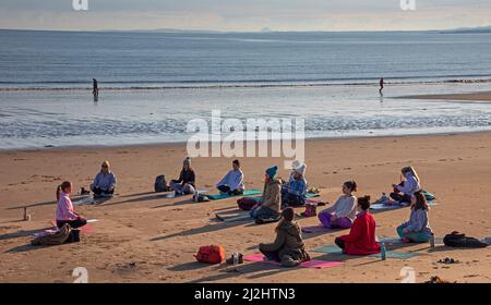 Portobello, Edinburgh Schottland, Großbritannien. April 2022. Erste Beach Yoga Klasse von 2022 am Meer neben dem Firth of Forth. Die Temperatur beträgt etwa 5 Grad Celsius, aber die Sonne gab der harten Gruppe Wärme. Stockfoto