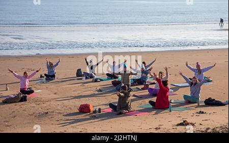 Portobello, Edinburgh Schottland, Großbritannien. April 2022. Erste Beach Yoga Klasse von 2022 am Meer neben dem Firth of Forth. Die Temperatur beträgt etwa 5 Grad Celsius, aber die Sonne gab der harten Gruppe Wärme. Stockfoto