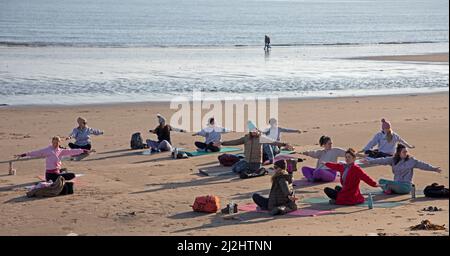 Portobello, Edinburgh Schottland, Großbritannien. April 2022. Erste Beach Yoga Klasse von 2022 am Meer neben dem Firth of Forth. Die Temperatur beträgt etwa 5 Grad Celsius, aber die Sonne gab der harten Gruppe Wärme. Stockfoto