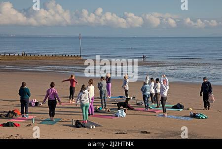 Portobello, Edinburgh Schottland, Großbritannien. April 2022. Erste Beach Yoga Klasse von 2022 am Meer neben dem Firth of Forth. Die Temperatur beträgt etwa 5 Grad Celsius, aber die Sonne gab der harten Gruppe Wärme. Stockfoto