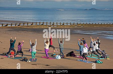 Portobello, Edinburgh Schottland, Großbritannien. April 2022. Erste Beach Yoga Klasse von 2022 am Meer neben dem Firth of Forth. Die Temperatur beträgt etwa 5 Grad Celsius, aber die Sonne gab der harten Gruppe Wärme. Stockfoto