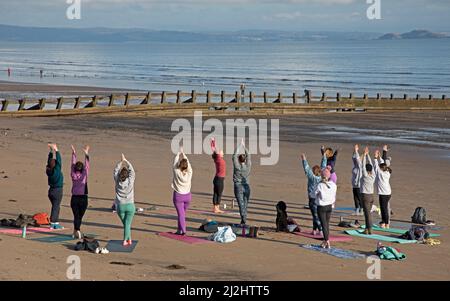 Portobello, Edinburgh Schottland, Großbritannien. April 2022. Erste Beach Yoga Klasse von 2022 am Meer neben dem Firth of Forth. Die Temperatur beträgt etwa 5 Grad Celsius, aber die Sonne gab der harten Gruppe Wärme. Stockfoto