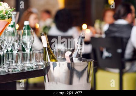 Die Leute im Restaurant. Zusammensetzung vieler Weingläser und Champagnerflaschen im Eimer auf dem Partytisch Stockfoto