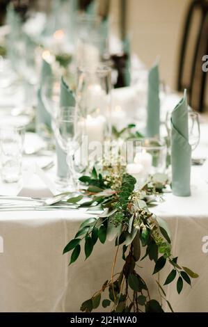 Elegante Tischeinstellung im Restaurant. Hochzeitsbankett mit Blumendekor auf dem Tisch, naturgrüner Zweig aus der Nähe Stockfoto