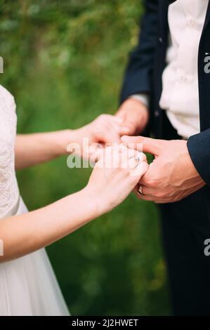 Hochzeitskonzept. Braut und Bräutigam halten die Hände Nahaufnahme auf grünem Gras Hintergrund. Eheringe Stockfoto