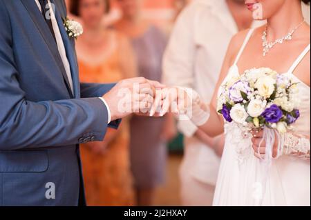 Hochzeitszeremonie. Bräutigam legt den goldenen Ring aus der Nähe auf den Finger der Braut. Eheringe tauschen das Gelübde. Stockfoto