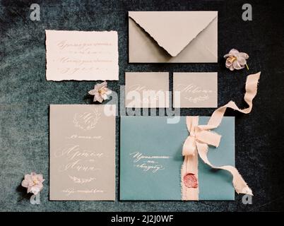 Set aus Hochzeitseinladungen und Kalligraphiekarten, Pfirsichbändern und Blumen auf dunkelgrauem Hintergrund. Draufsicht, flach liegend Stockfoto