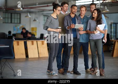 HES hat den Plan für den Tag erhalten. Eine Gruppe von Kollegen, die spontan mit einem digitalen Tablet in einem offenen Büro zusammentreffen. Stockfoto