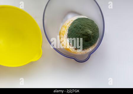 Zitrone mit schimmelig-grünem, abgeschnittener Schale in Form eines Deckels in einem offenen Behälter für Zitronen Stockfoto