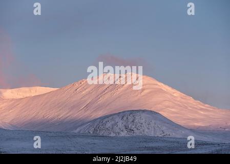 Wunderschöne Alpen Glow treffen Berggipfel in den schottischen Highlands während des atemberaubenden Sonnenaufgangs in der Winterlandschaft Stockfoto