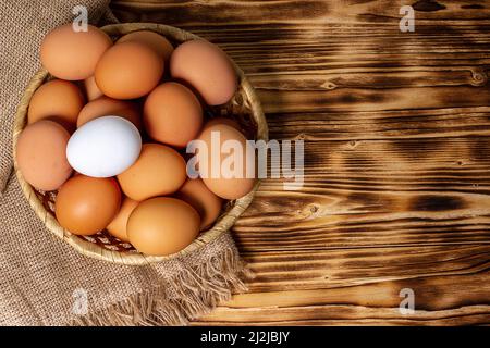 Huhn Eier im Korb auf eine Serviette von sackleinen auf hölzernen Tisch. Ansicht von oben. Rustikales essen Hintergrund Stockfoto