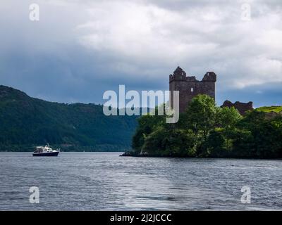 Ein Boot fährt am Urquhart Castle vorbei, das in Ruinen auf Strone Point oberhalb von Loch Ness in der Nähe von Drumnadrochit, Schottland, Großbritannien, steht. Stockfoto